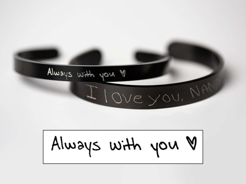 Two black stainless steel bracelets engraved with silver handwriting saying "Always with you" and "I love you, Nana"